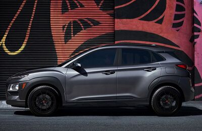 A side view of a dark gray Hyundai Kona parked in front of a wall with colorful graffiti art.