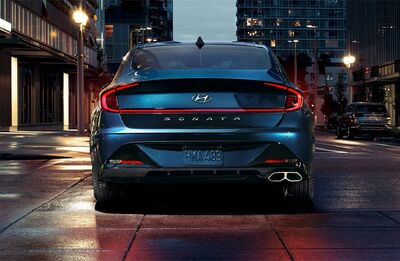 Rear view of a dark blue Hyundai Sonata parked on a city street at night.