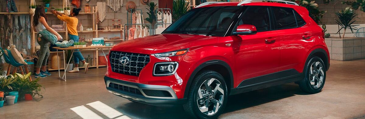 A red Hyundai Venue parked in a garage with people in the background.