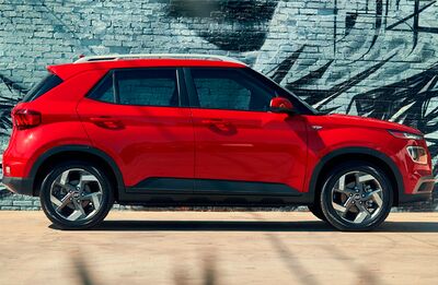 A red Hyundai Venue parked in front of a graffiti-covered brick wall.