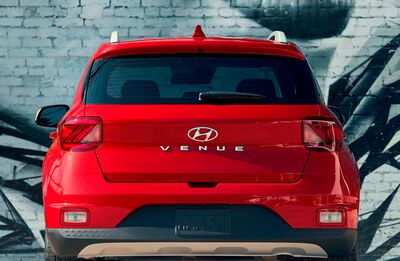 The back of a red Hyundai Venue parked in front of a graffiti-covered brick wall.