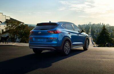 Rear view of a blue Hyundai Tucson driving on a city street.