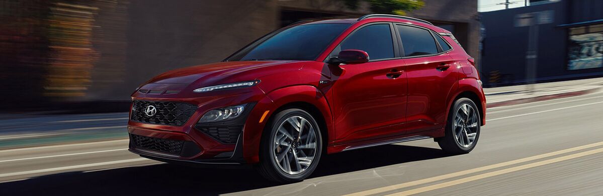 A red Hyundai Kona driving down a city street.