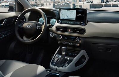 The interior of a Hyundai Kona, showing the driver's seat, steering wheel, and a center console with a touchscreen display.
