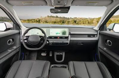 The interior of a car with two seats, a steering wheel, and a large touchscreen display.