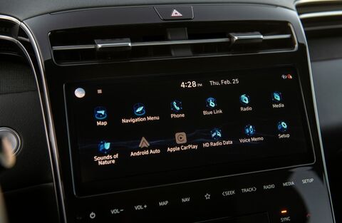 A close-up of the infotainment system screen in a Hyundai Tucson. The screen displays various icons for features like navigation, phone, music, and voice control.