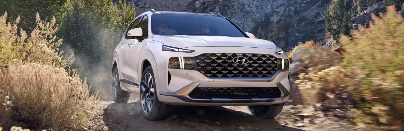 A white Hyundai Santa Fe driving confidently through a rugged, off-road terrain.