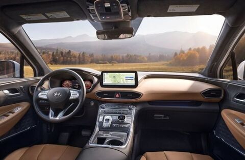 The interior of a Hyundai Santa Fe, showing the driver's seat, steering wheel, and dashboard with a large touchscreen display. A scenic landscape is visible through the windshield.