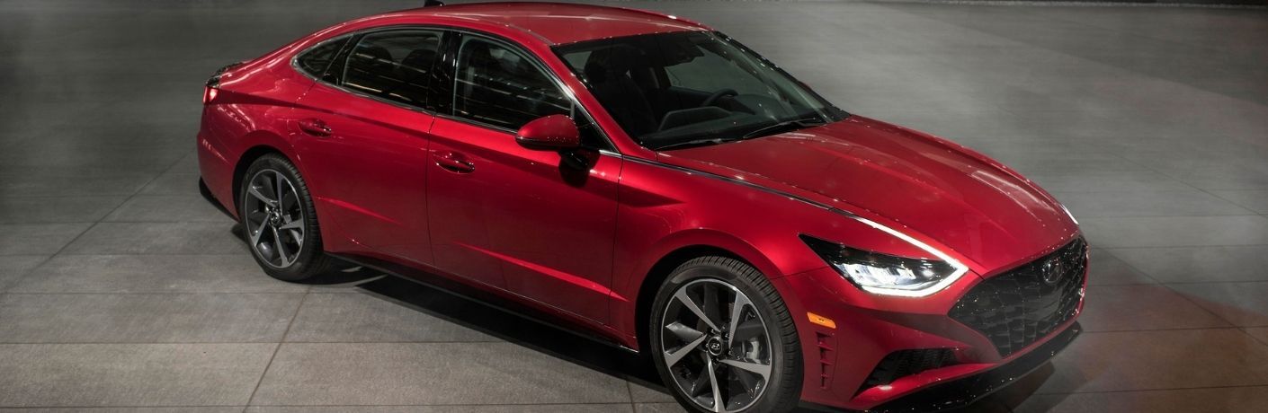 A red Hyundai Sonata, parked on a concrete surface. The car is shown from a three-quarter angle, highlighting its sleek design and sporty lines.
