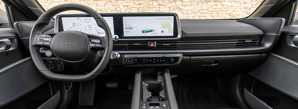 The interior of a Hyundai Ioniq 6, showcasing the driver's perspective. The image highlights the steering wheel, dashboard with a large curved touchscreen display, and a digital instrument cluster.