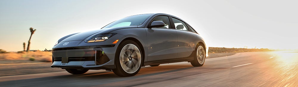 A silver Hyundai Ioniq 6 driving on a desert highway at sunset.