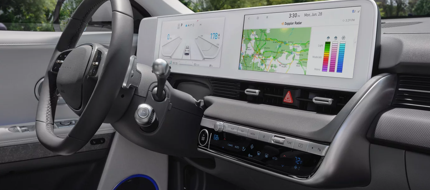 The interior of a Hyundai Ioniq 5, showcasing a large, curved touchscreen display that spans the width of the interior. The display houses the instrument cluster and infotainment system, with a map navigation interface visible on the screen.