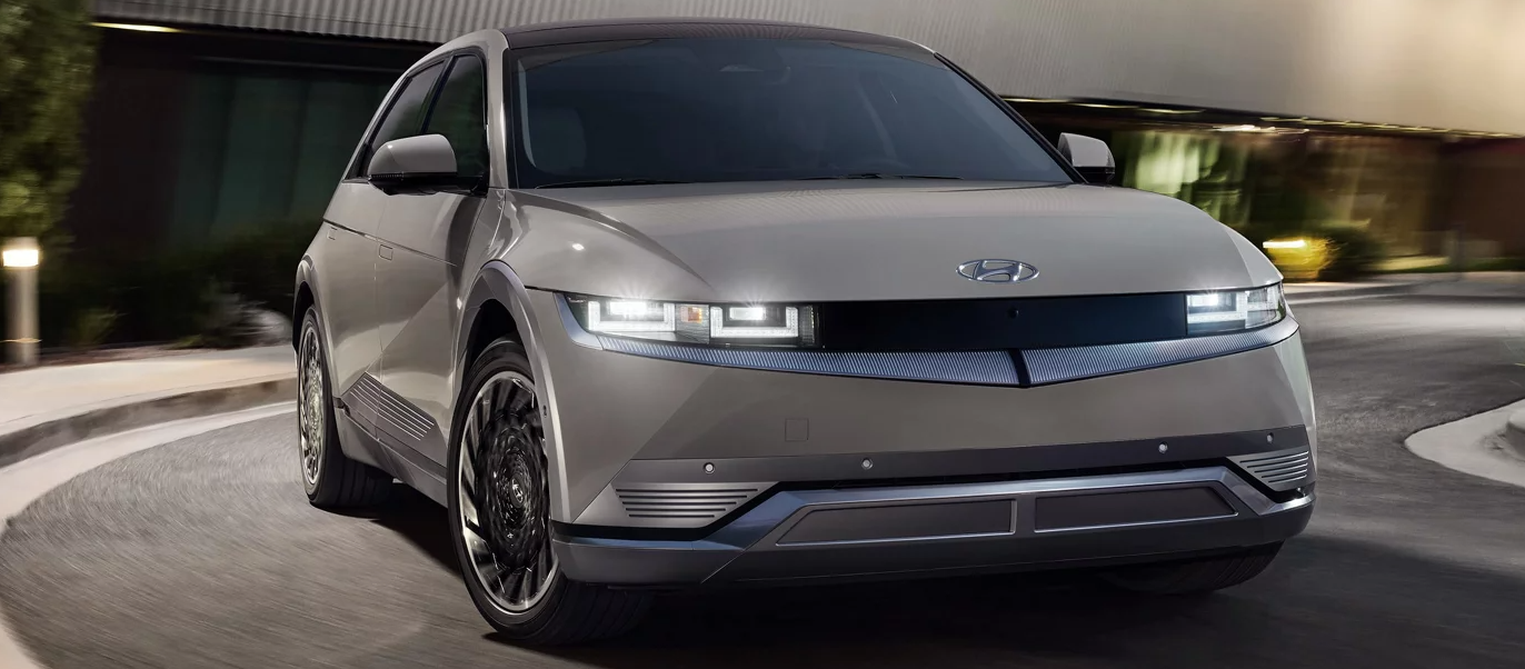 A silver Hyundai Ioniq 5 driving on a city street at night.