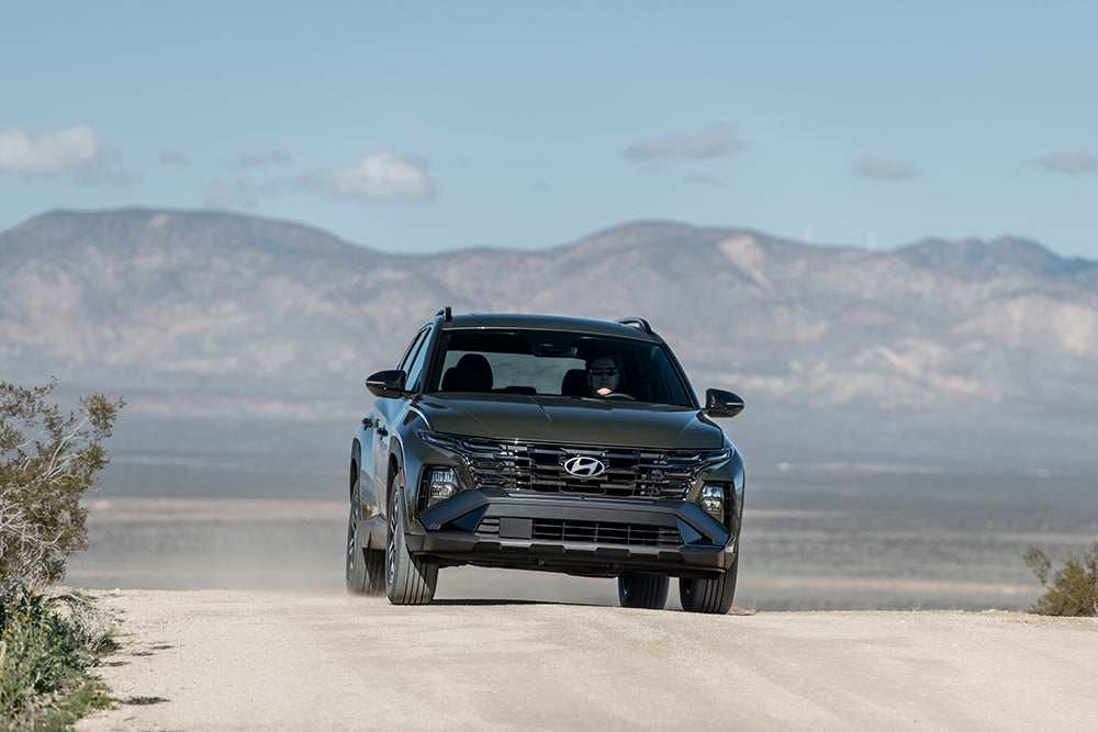 A dark-colored Hyundai Tucson SUV driving on a dusty trail in a desert landscape.