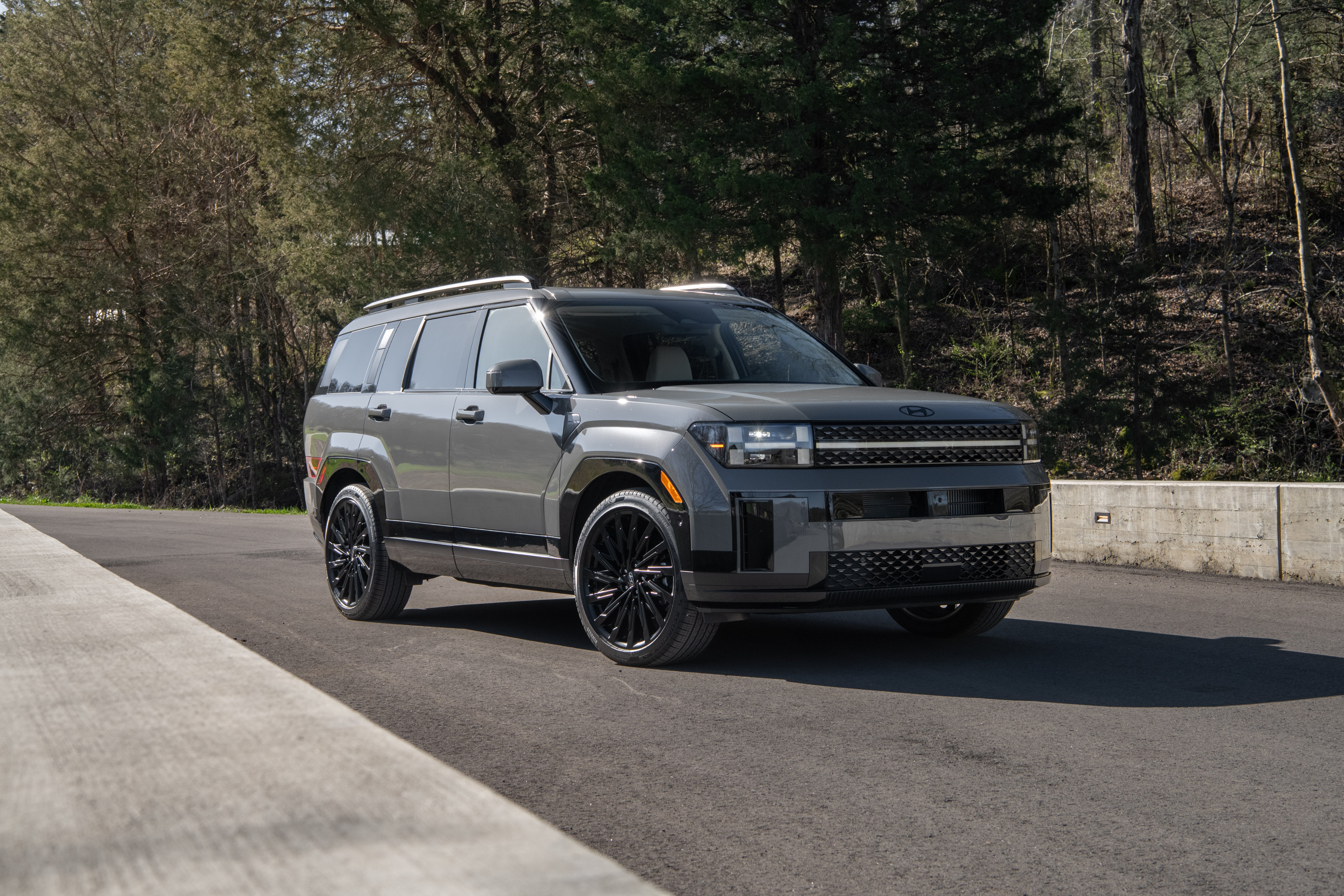 A grey Hyundai Santa Fe parked on a small road bridge over a creek in a forested area.