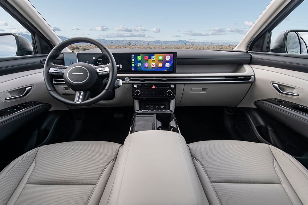 The interior of a Hyundai Tucson, showcasing the driver's perspective. The image highlights the steering wheel, dashboard with a large touchscreen display, and a digital instrument cluster.
