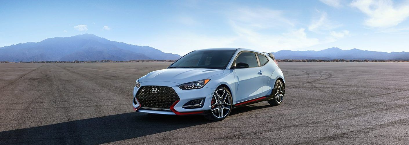 A white Hyundai Veloster N sports car parked on a race track with a mountain range in the background.