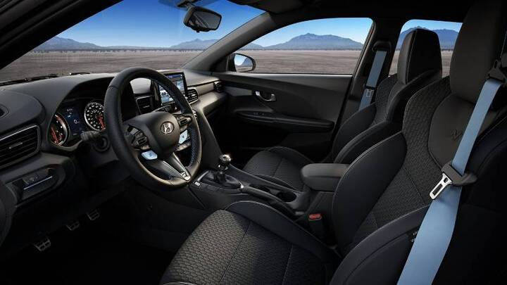 The interior of a Hyundai Kona N, showing the driver and passenger seats with sporty bucket-style design and contrasting blue accents on the seatbelts.
