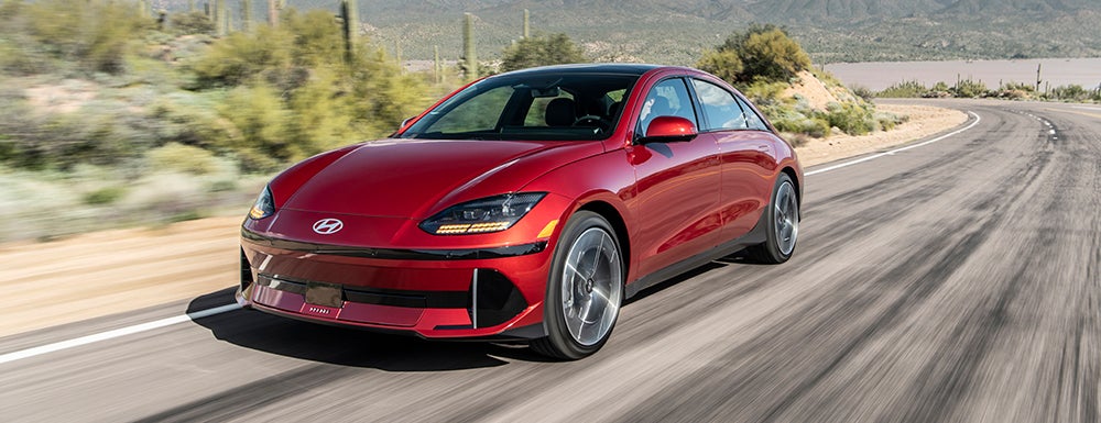 A red Hyundai IONIQ 6 electric sedan in motion on a scenic road with a desert landscape.