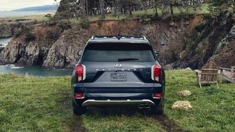 A dark blue Hyundai Palisade parked on a grassy cliff overlooking a scenic coastline. The SUV's rear end is visible, showcasing its distinctive taillights and "Palisade" badge.
