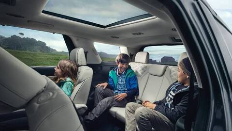 A man in a yellow raincoat is standing next to a dark blue Hyundai Palisade. The SUV's rear hatch is open, revealing a spacious cargo area filled with luggage and camping gear.