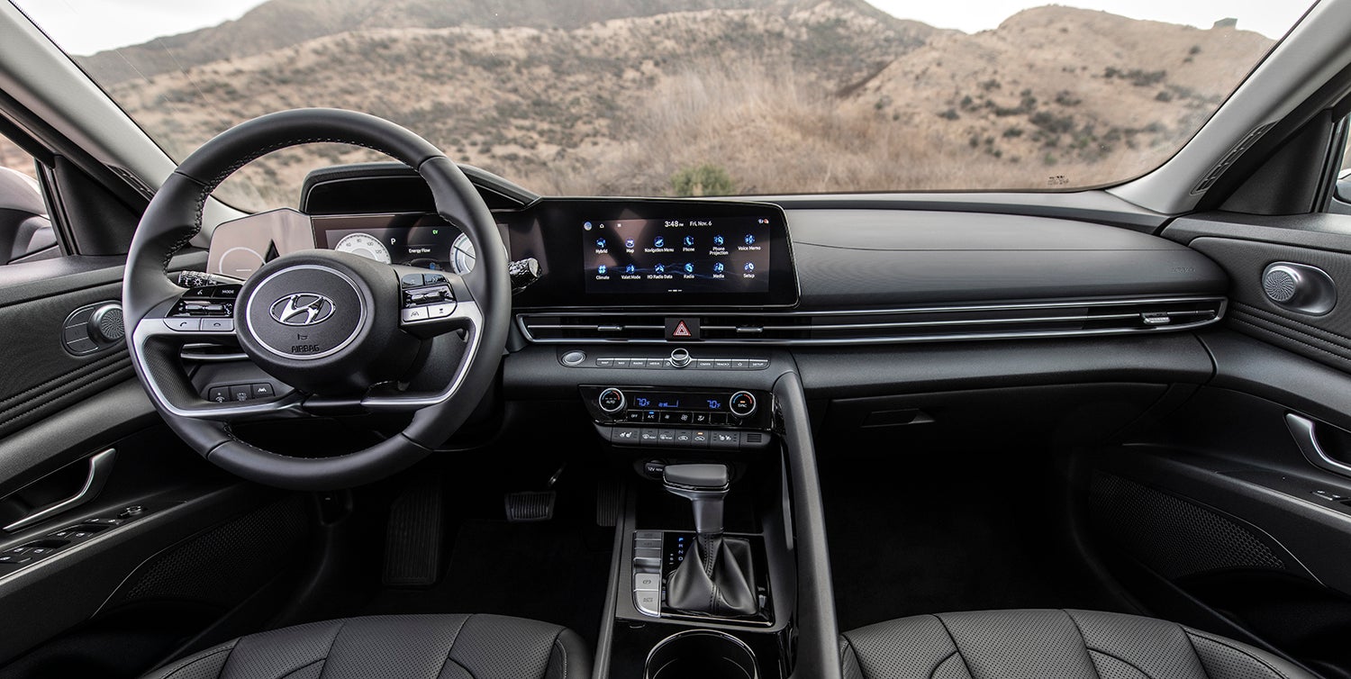 The interior of a Hyundai Elantra, showing the driver's seat, steering wheel, and dashboard with a large touchscreen display.