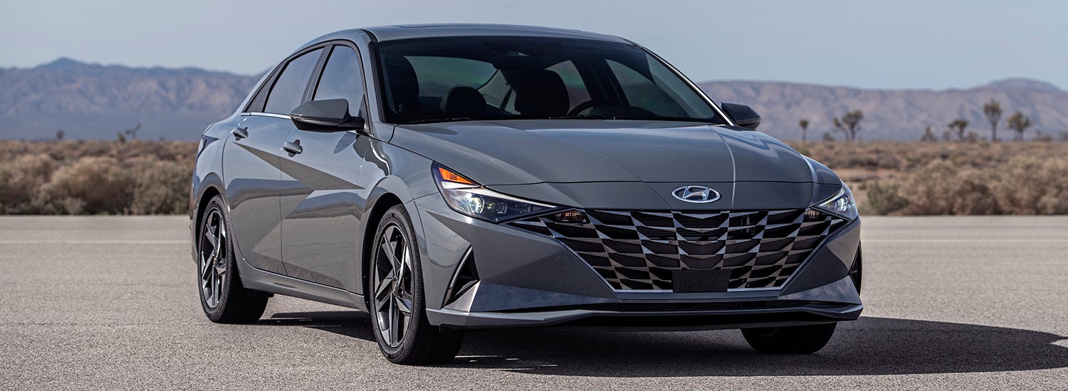 A gray Hyundai Elantra parked on a desert road with mountains in the background.