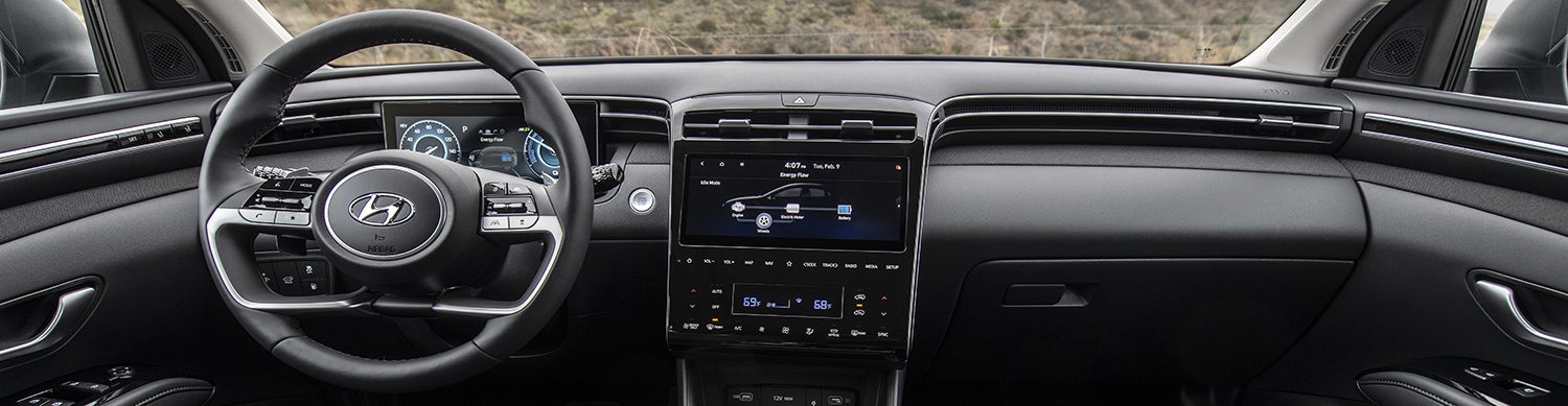 The interior of a Hyundai Tucson Hybrid, showing the driver's seat, steering wheel, and dashboard with a large touchscreen display.