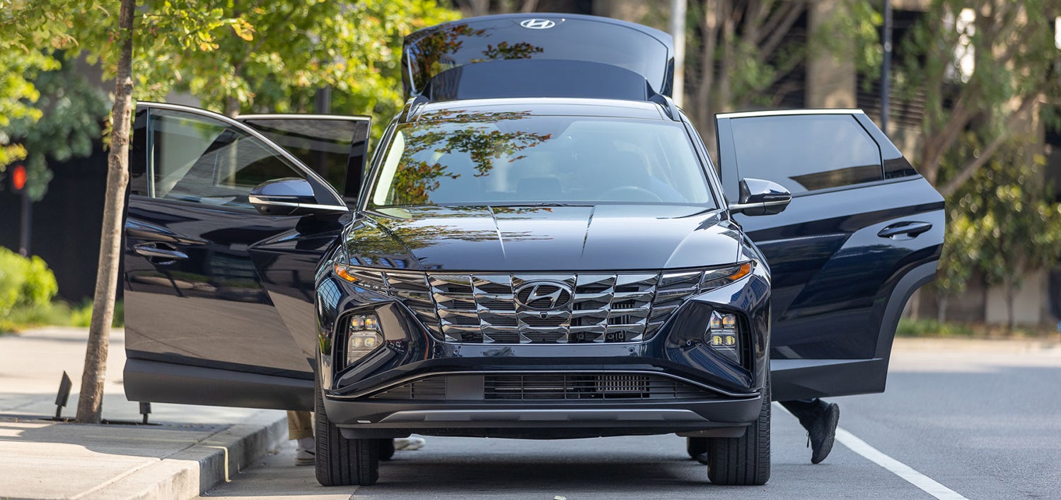 A black Hyundai Tucson parked on a city street with its front doors and hood open.