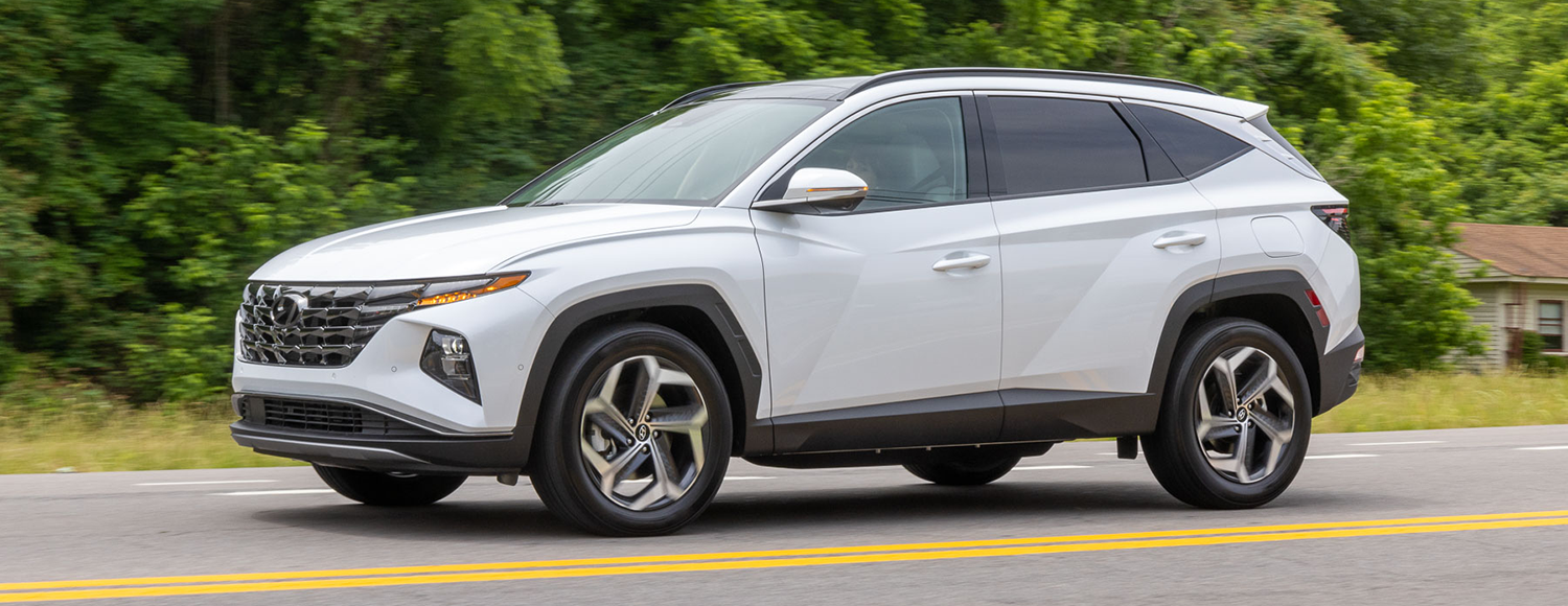 A white Hyundai Tucson driving on a winding road through a lush green forest.